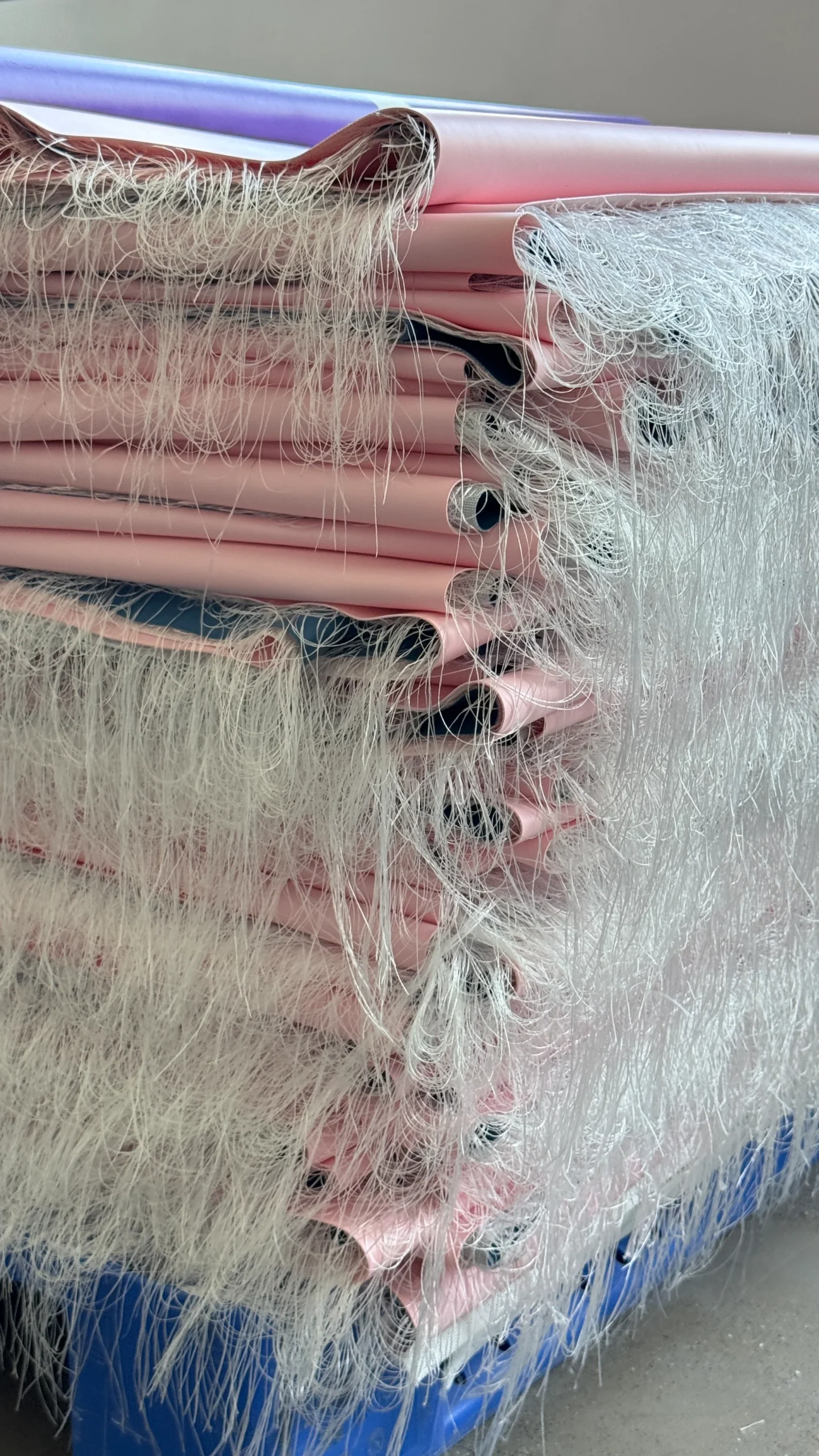 A stack of pink fabric rolls with white fringes on the edges, neatly piled together.