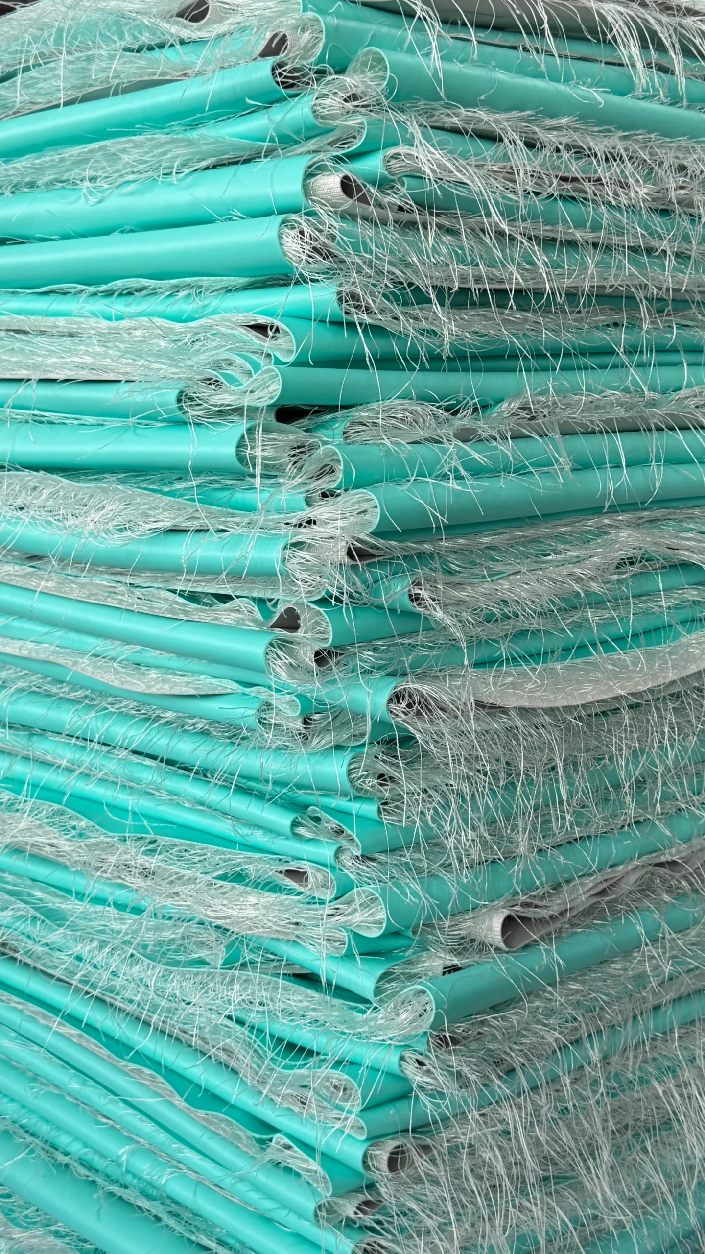 Neatly stacked rolls of aqua-colored PVC sheets threaded with fibrous fiberglass strands.