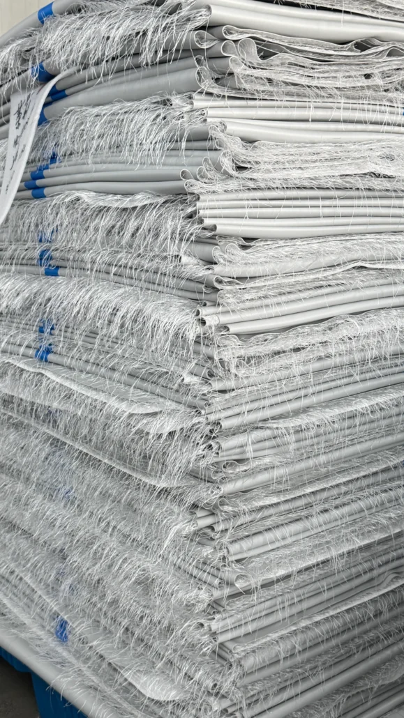 A large stack of rolled fiber mattresses with synthetic fibers visible, organized neatly in a storage area.