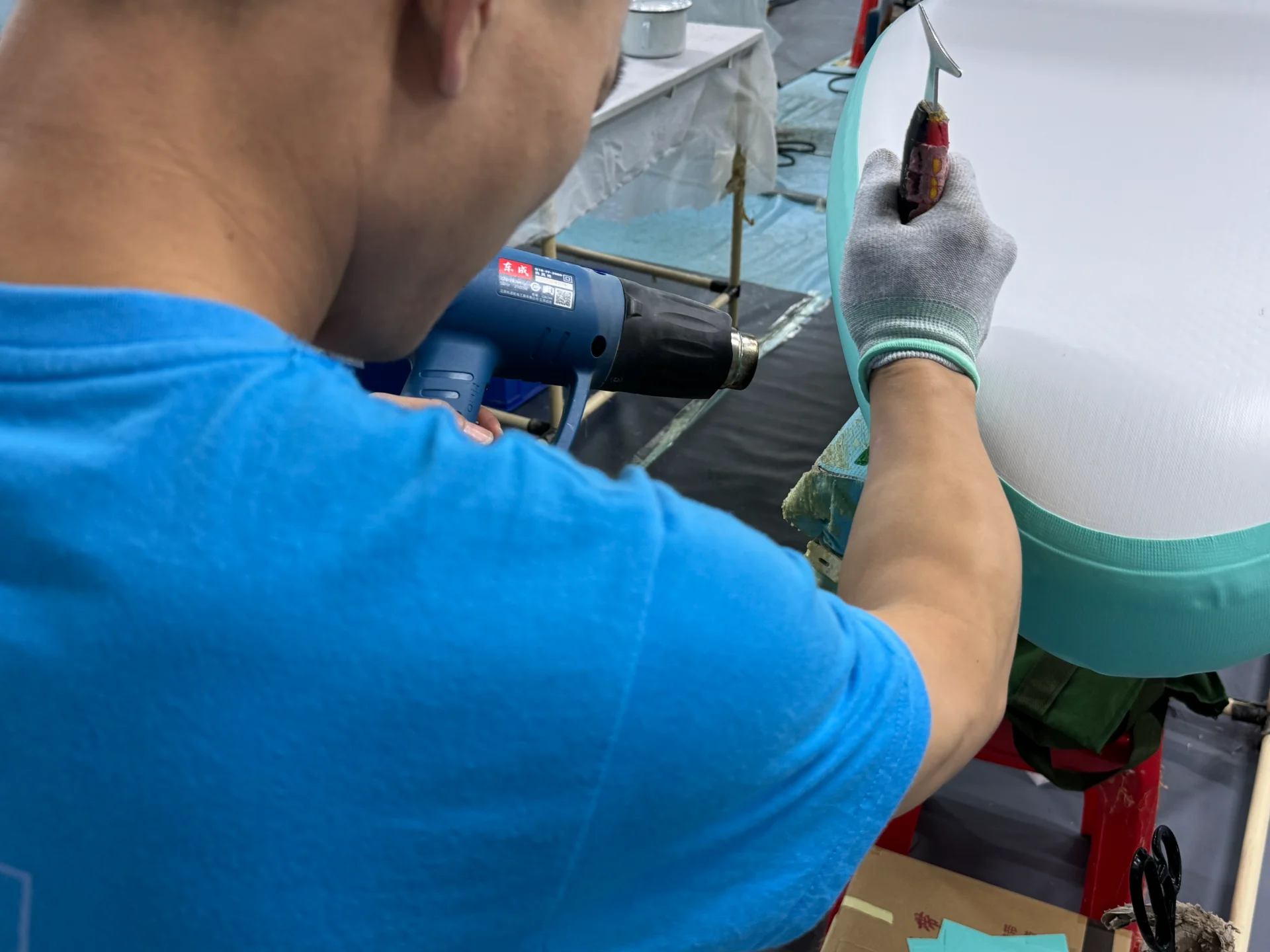 Man in a blue shirt using a heat gun and a tool on a cushion, focused on upholstery work.