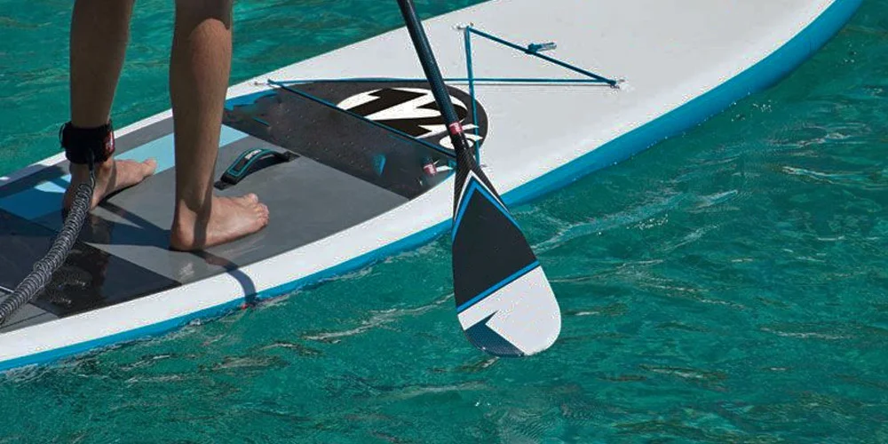 Close-up of a person stand-up paddleboarding, showing their feet on the board and a paddle touching clear turquoise water.