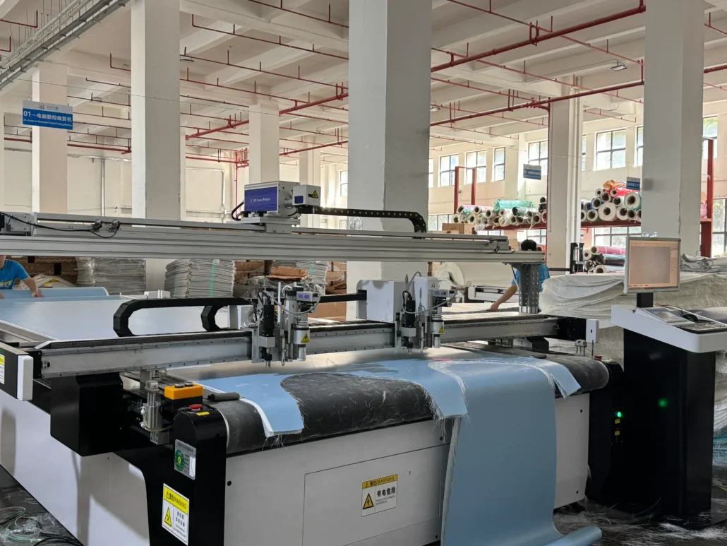 Automated machinery with computer control in a textile factory handling fabric rolls, surrounded by stacks and windows.