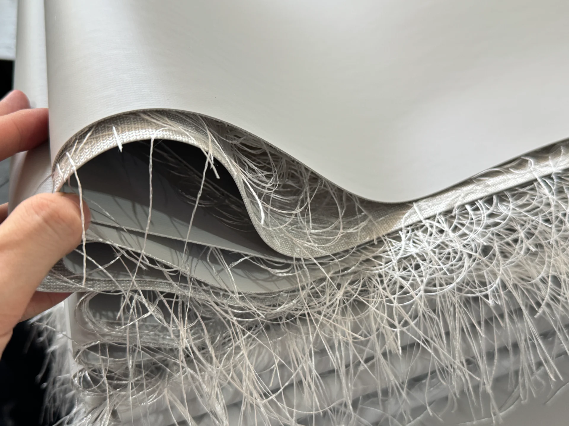 Close-up of rolled fiberglass material with visible fibers and strands, held by a hand, showing the texture and structure.