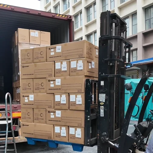 Forklift loading multiple cardboard boxes into a large shipping container, with background of a building.
