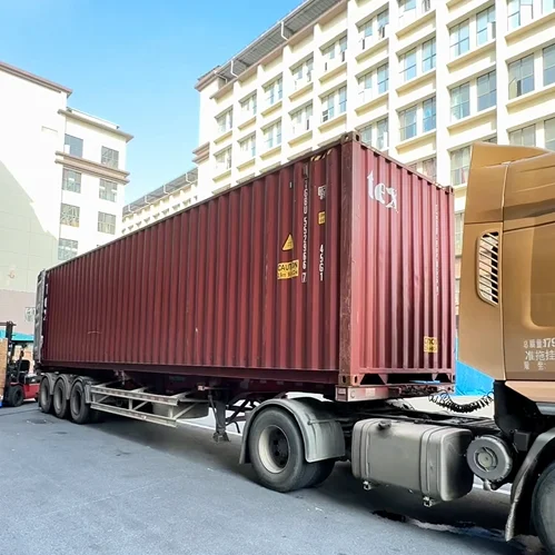 Red shipping container mounted on a truck parked beside a building under a clear blue sky.