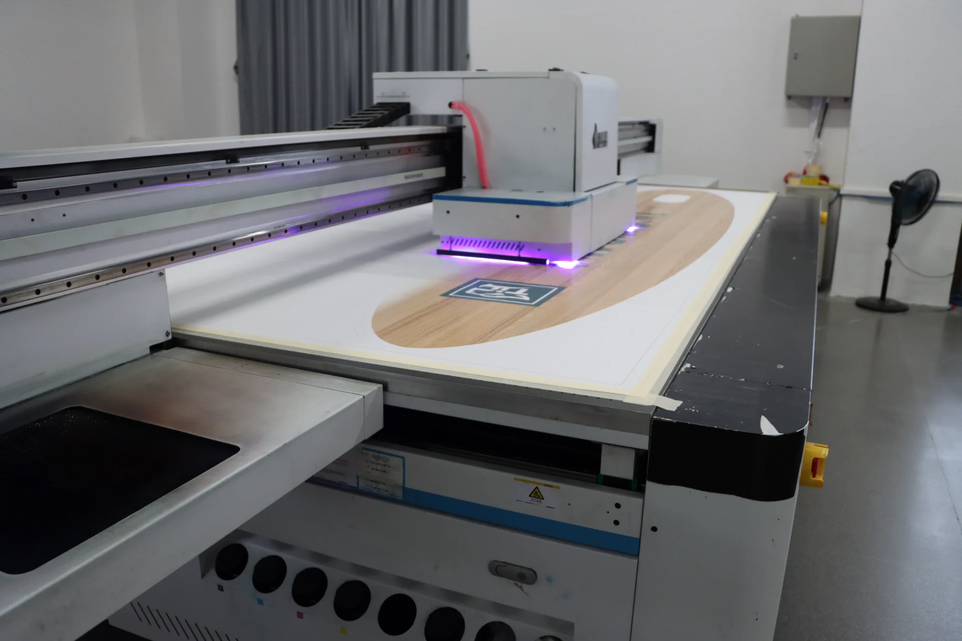 UV printer in operation, printing a large format image with purple UV lights on white material in a workshop.