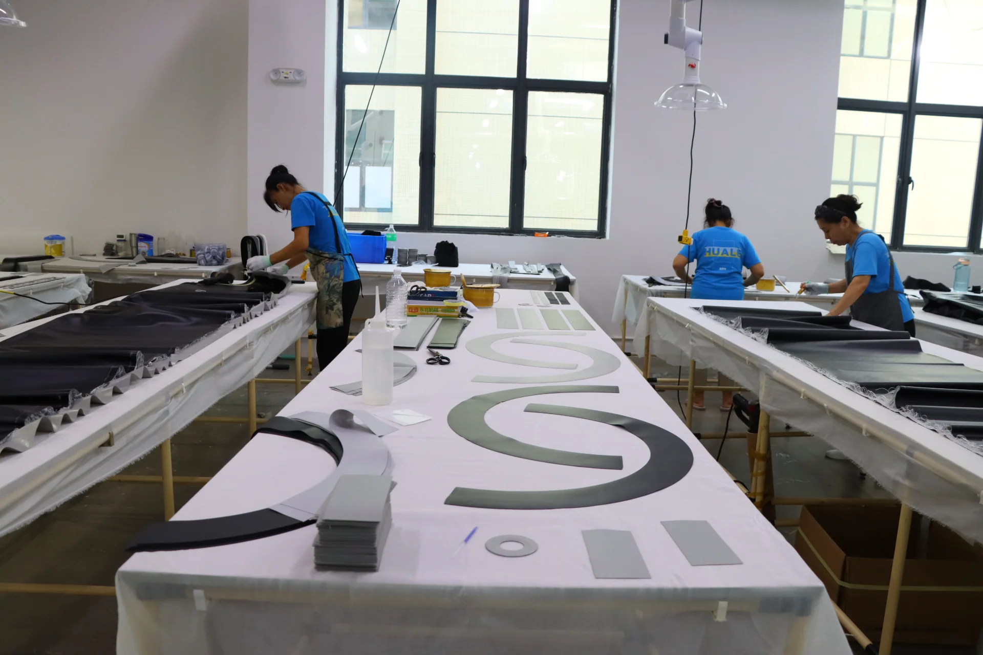 People working at tables in a fabrication lab, cutting and organizing various materials in a bright room.