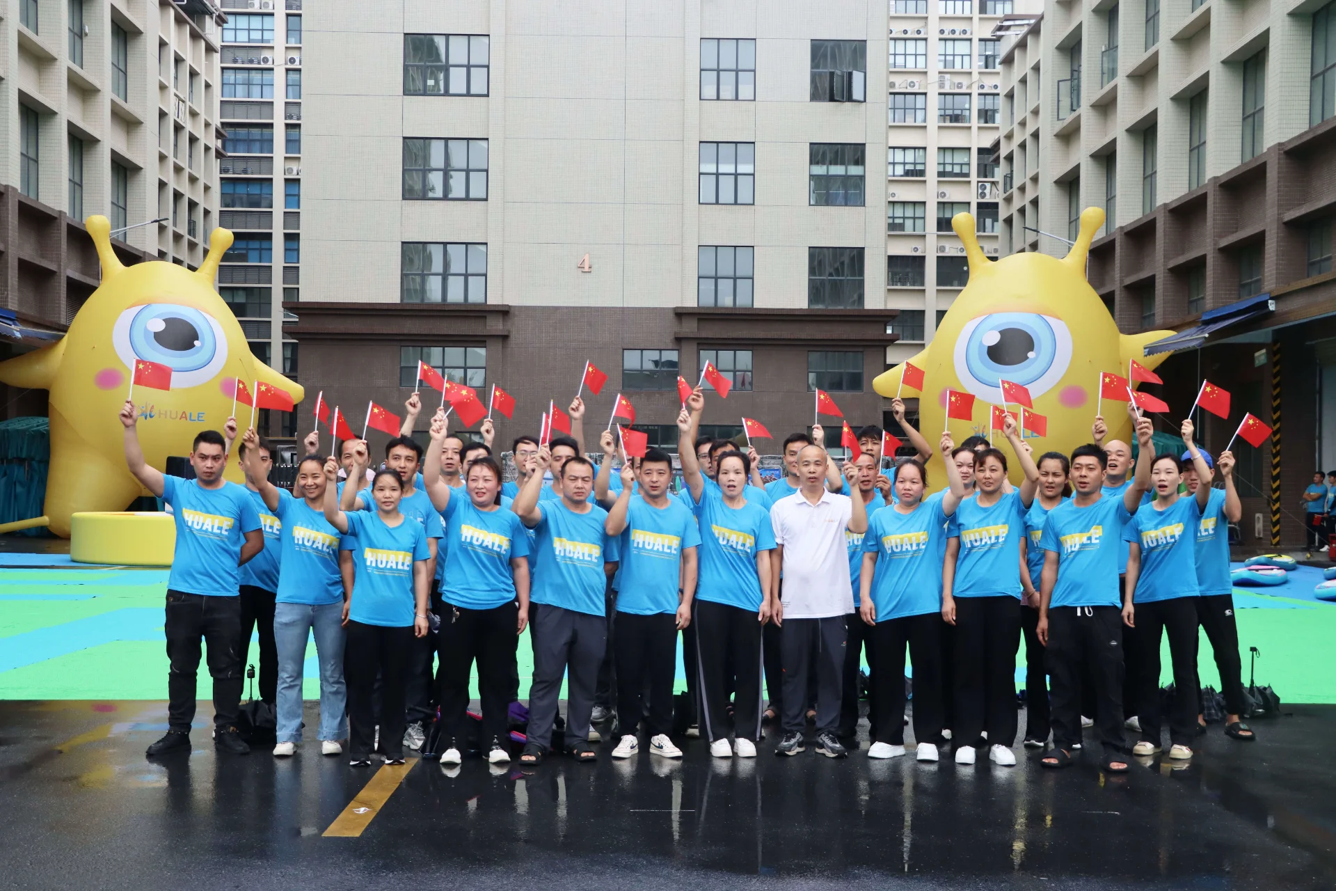 A group of people wearing blue shirts hold Chinese flags, standing in front of inflatable yellow characters outdoors.