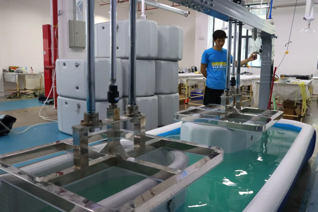 Industrial machinery next to a water tank in a factory, featuring stacks of white containers and metal framework.