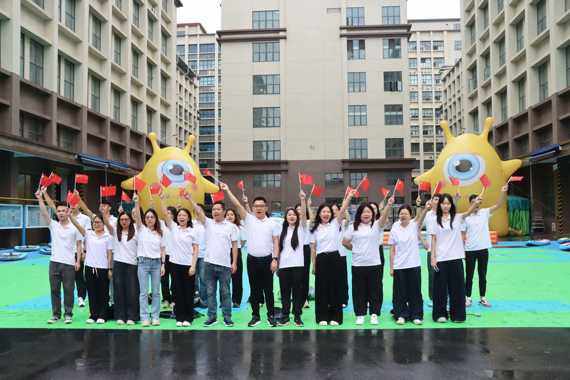 A group of people in white shirts holding small flags while standing in front of inflatable yellow characters at an outdoor event.