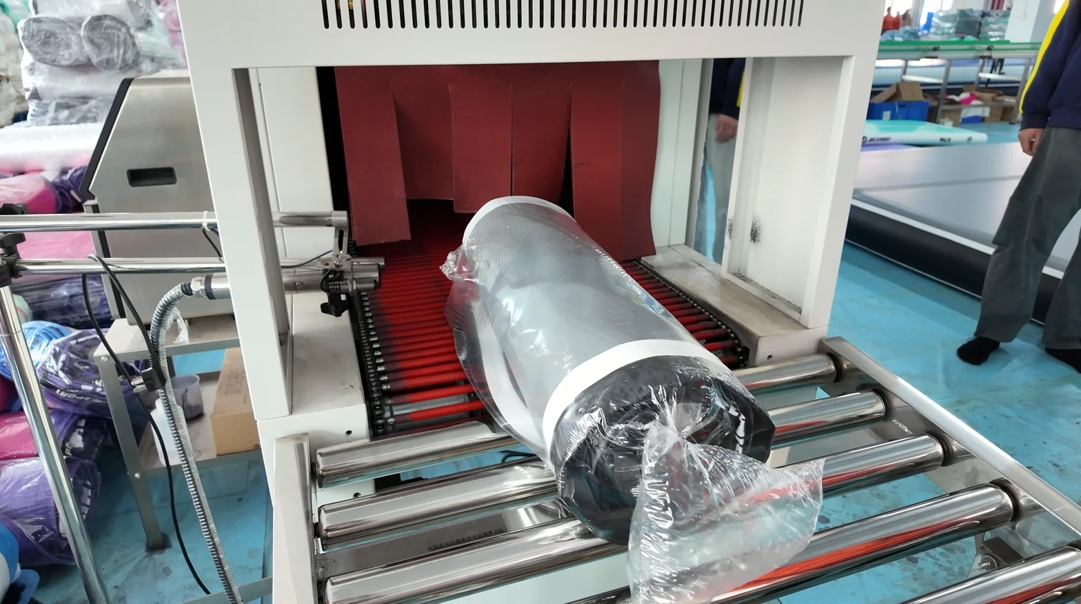 Plastic roll wrapped in film on conveyor belt entering an industrial packaging machine.