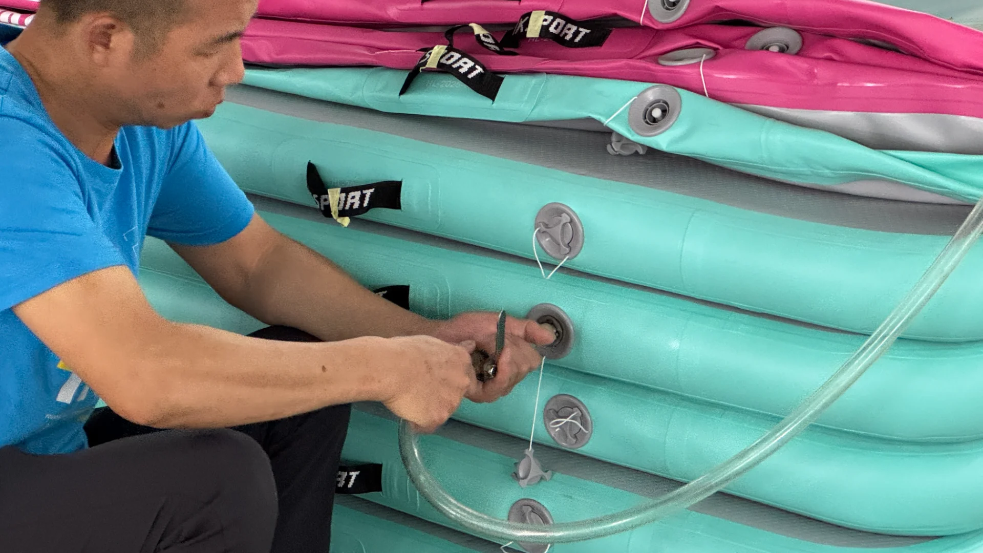 Person in blue shirt inflating a stack of turquoise and pink paddleboards using a pump.