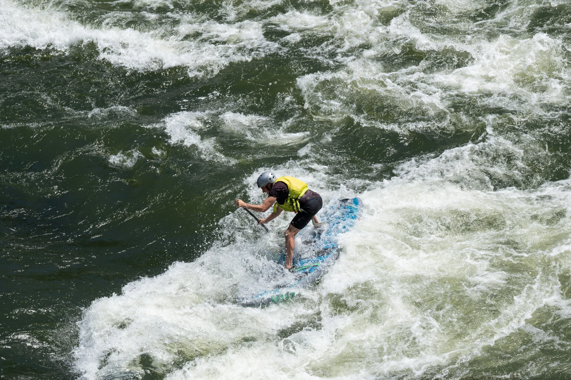 Person wearing helmet and life jacket paddling through rough rapids on a kayak.