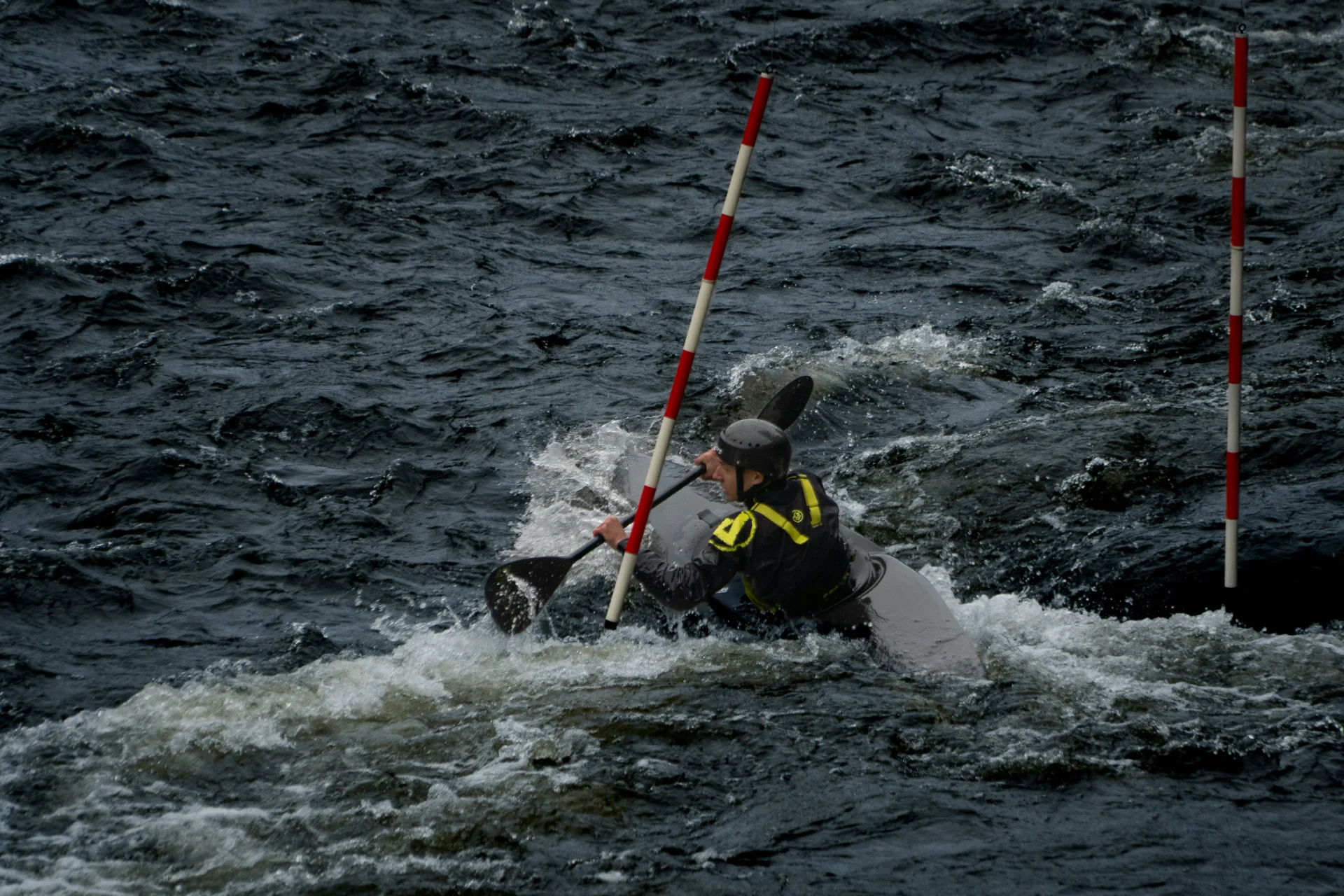 Kayaker skillfully paddling through slalom gates on choppy water, wearing a helmet and gear.