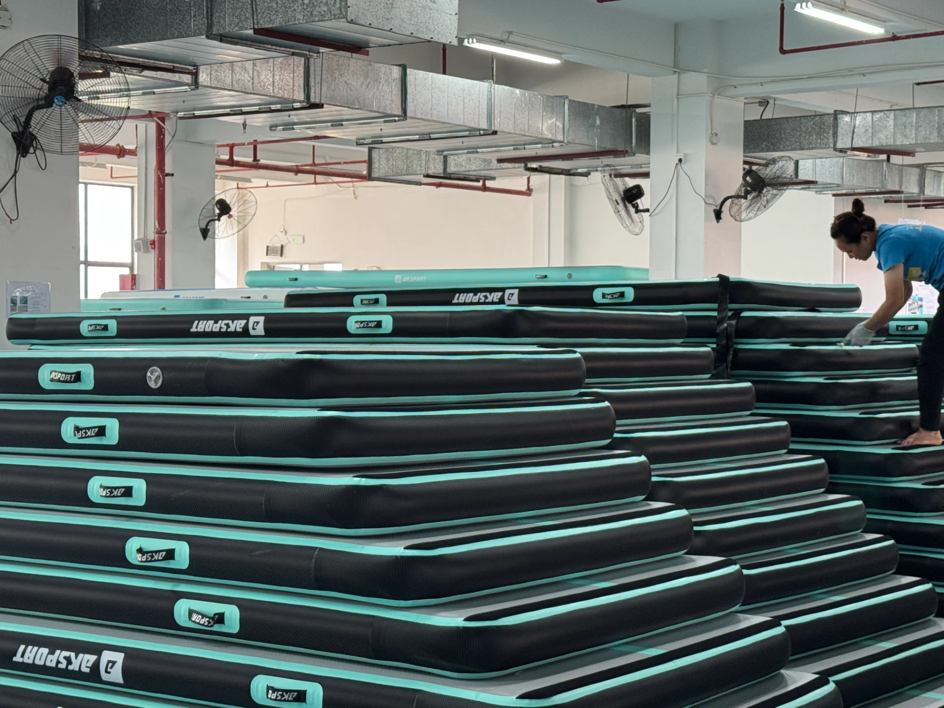Several inflatable mats stacked in layers within a factory environment, with a worker adjusting them.