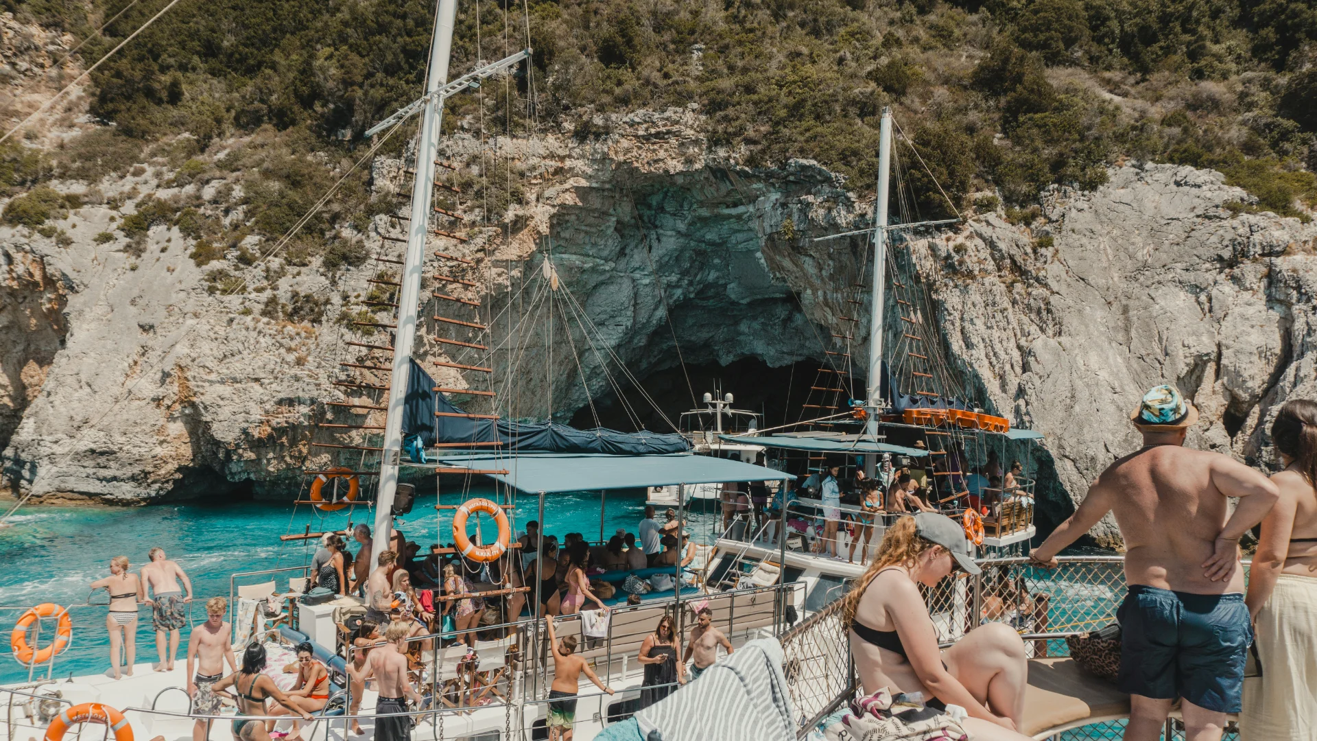 Tourists on a sailboat near a coastal cave with clear blue water, enjoying a sunny day trip and beautiful natural scenery.