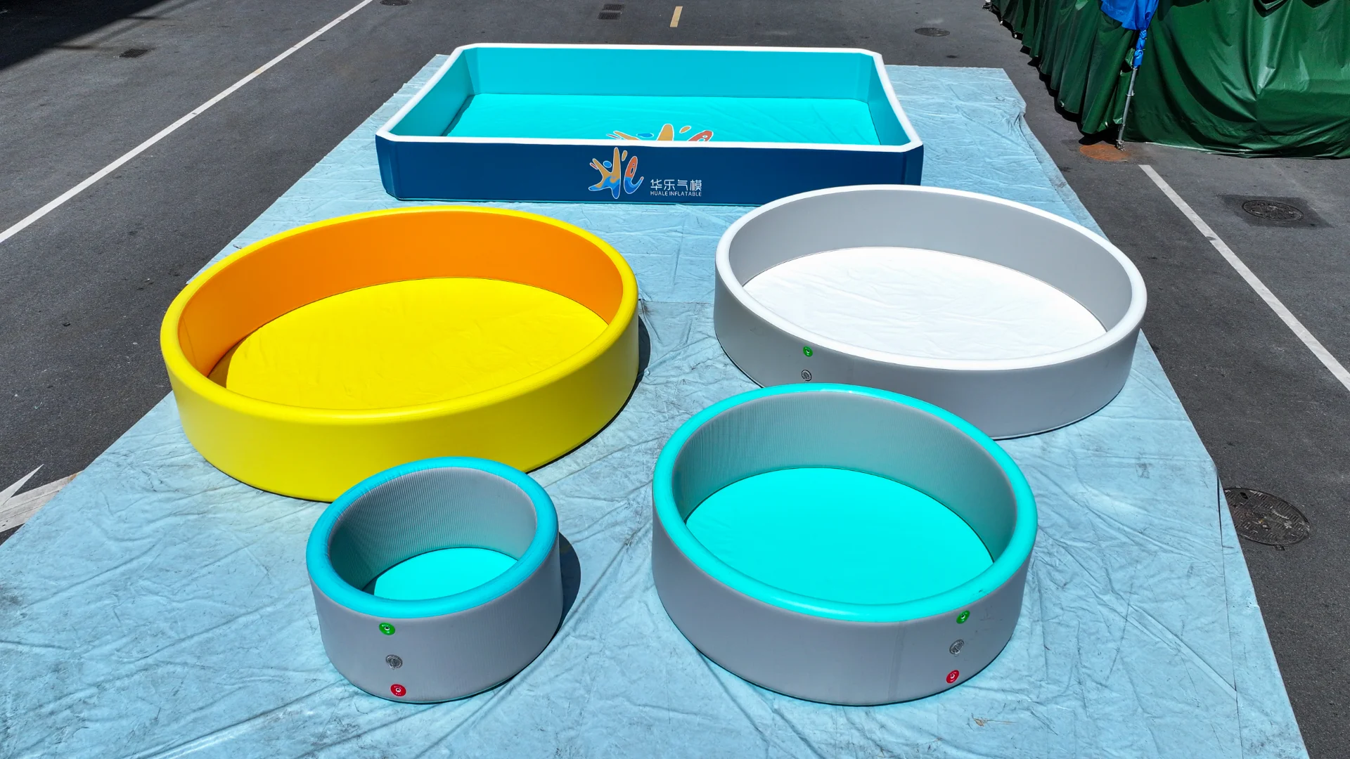 Five inflatable pools of varying sizes, including yellow, white, and blue, arranged on a blue tarp outdoors.