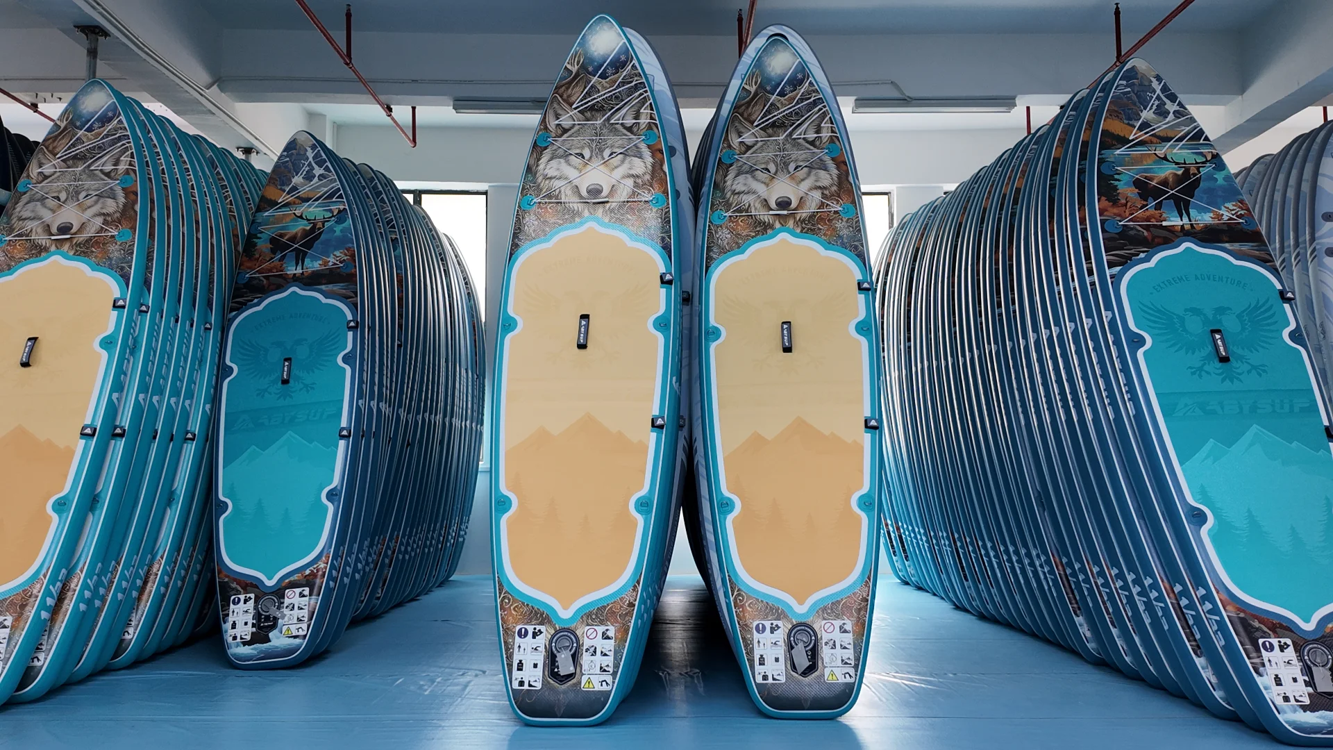 Multiple blue and beige paddleboards featuring a wolf design are stacked in a storage area.