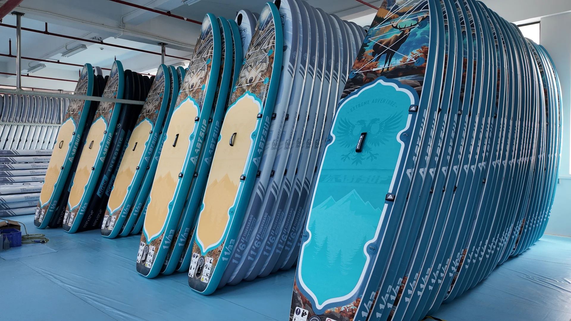 Several stacked inflatable paddleboards with colorful designs stored upright in a warehouse setting.