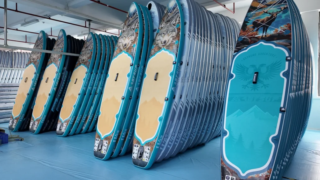 Stack of colorful paddleboards with artistic designs, lined up in a manufacturing facility.