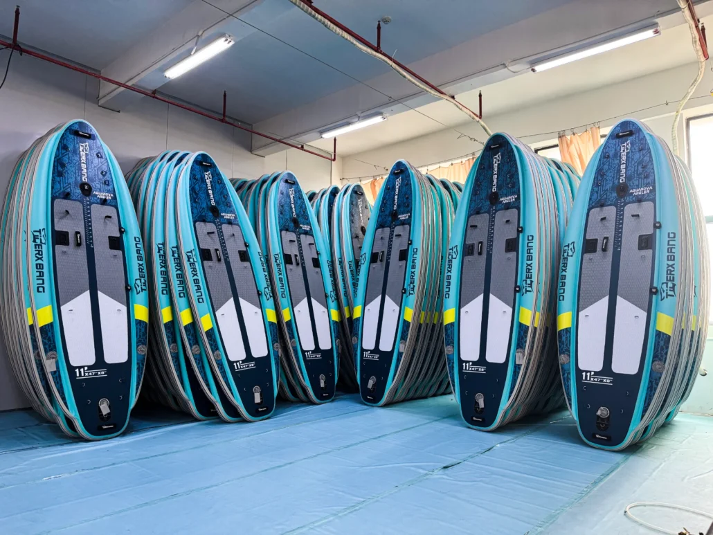 Rows of upright paddleboards stored indoors, with blue and white designs, organized side by side.