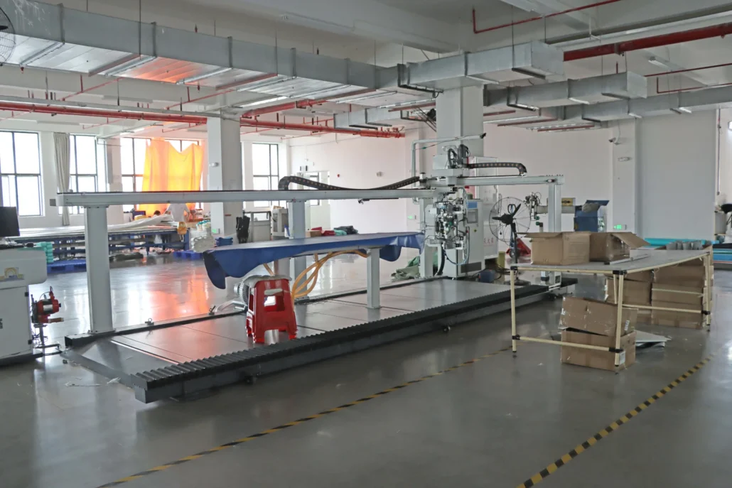 Large industrial machine in a factory setting with boxes and equipment on the floor, under fluorescent lighting.