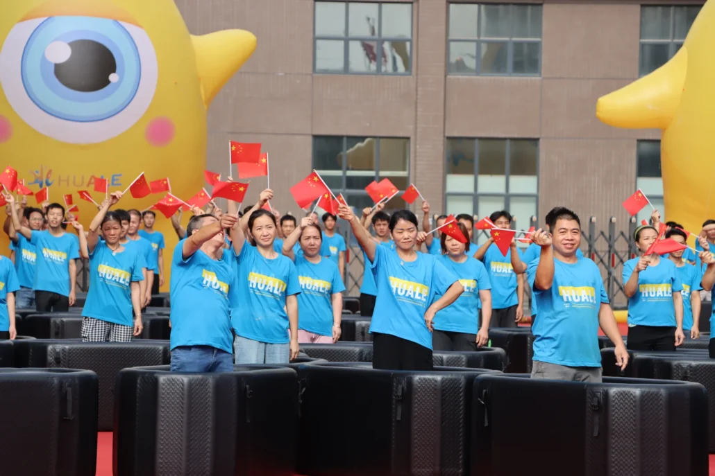 People in blue Huale shirts waving Chinese flags during an outdoor event, with a large inflatable yellow figure in the background.