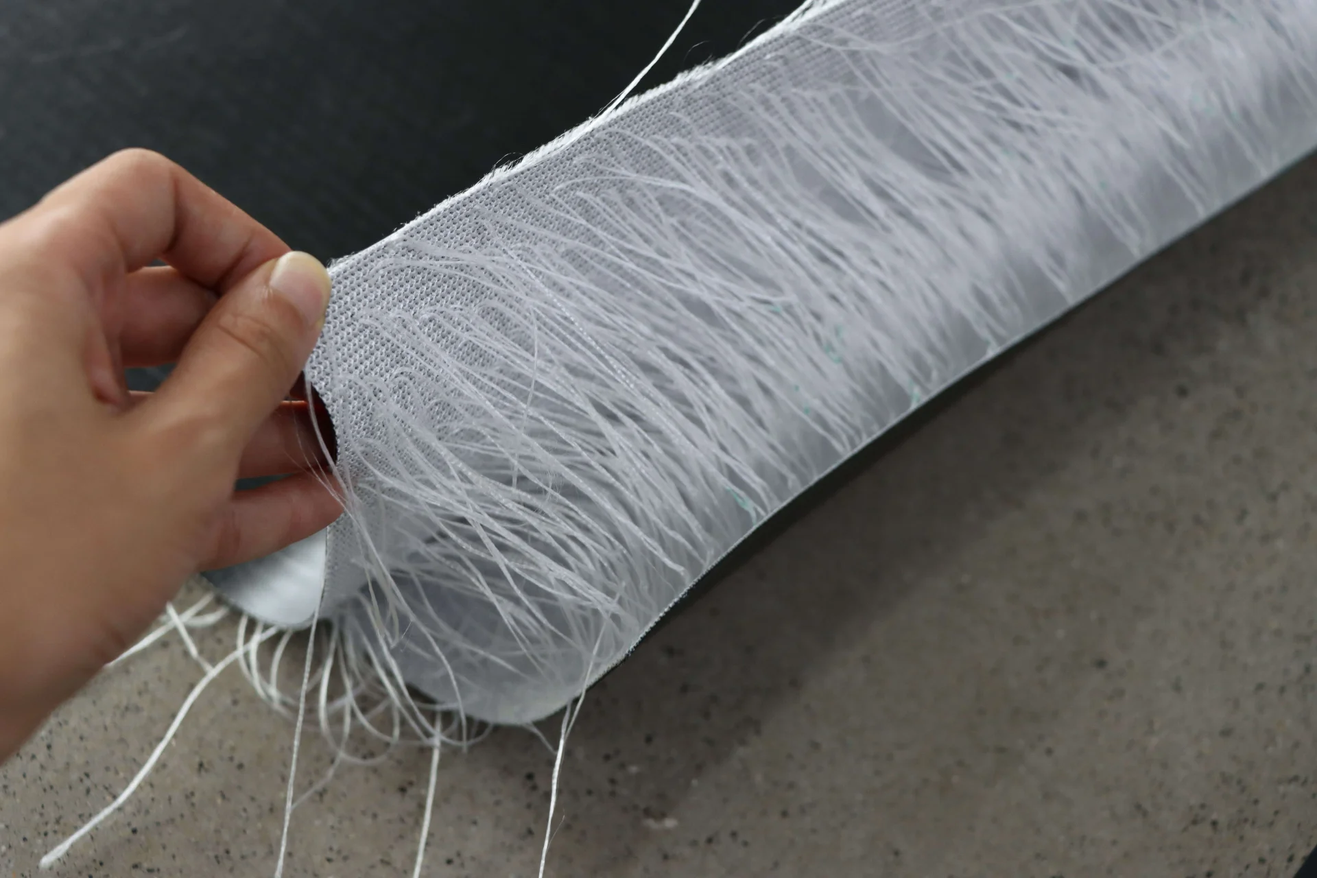 A hand gently holding a section of white fiberglass mesh roll with visible fine threads, laid on a solid surface.