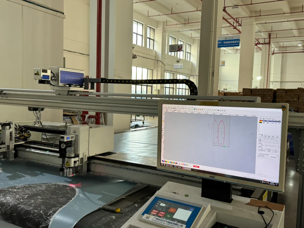 Industrial laser cutting machine operating in a factory with computer screen showing cutting design.