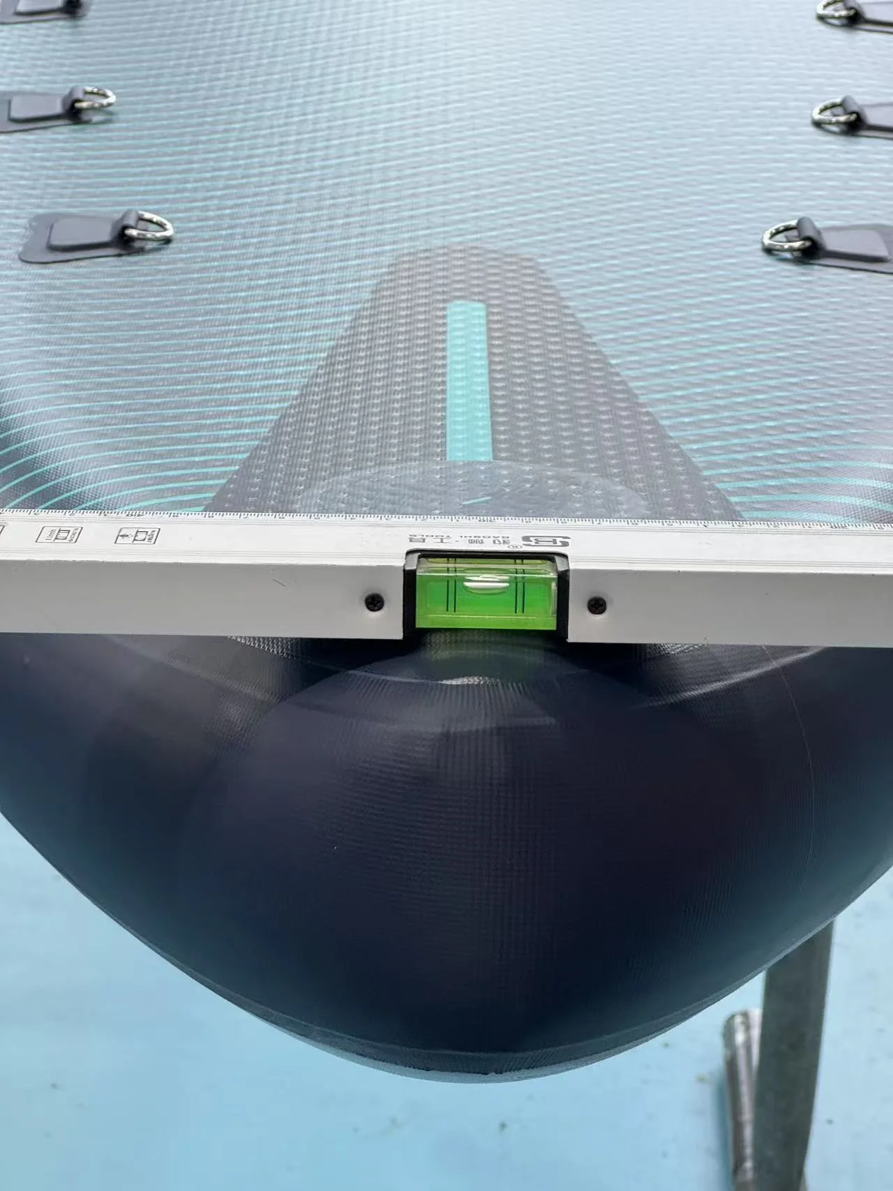 Level tool placed on the surface of an inflatable boat, checking for evenness. The boat has a textured pattern and metal loops.