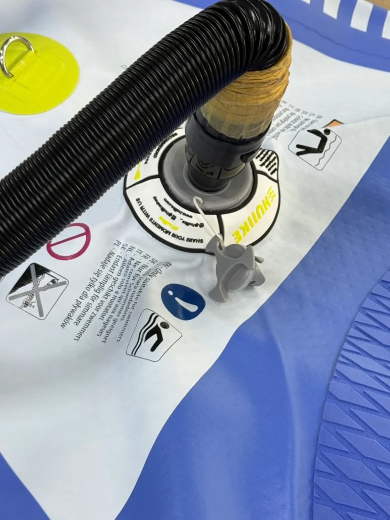 Close-up view of a pump valve on an inflatable paddleboard with a black hose attached, surrounded by safety instructions.