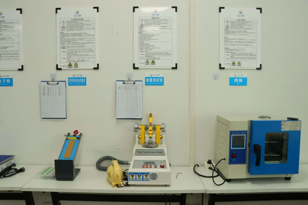 Various laboratory equipment including a Taber type abrasion tester and an oven, with instructions on the wall.
