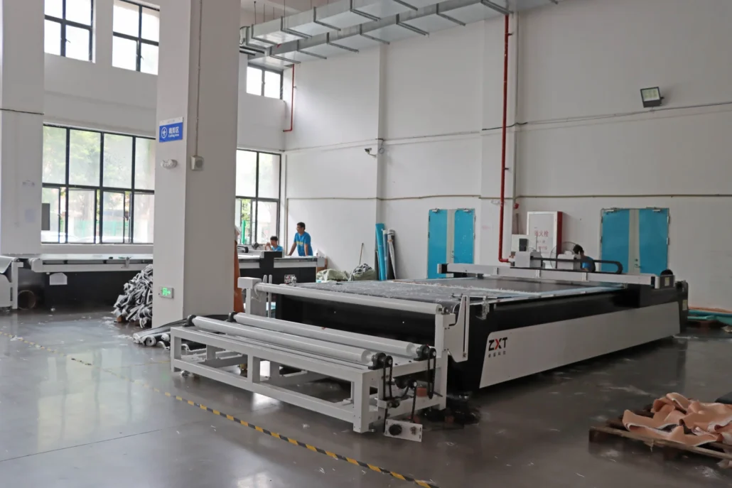 Large industrial cutting machine in a spacious workshop with workers in the background.