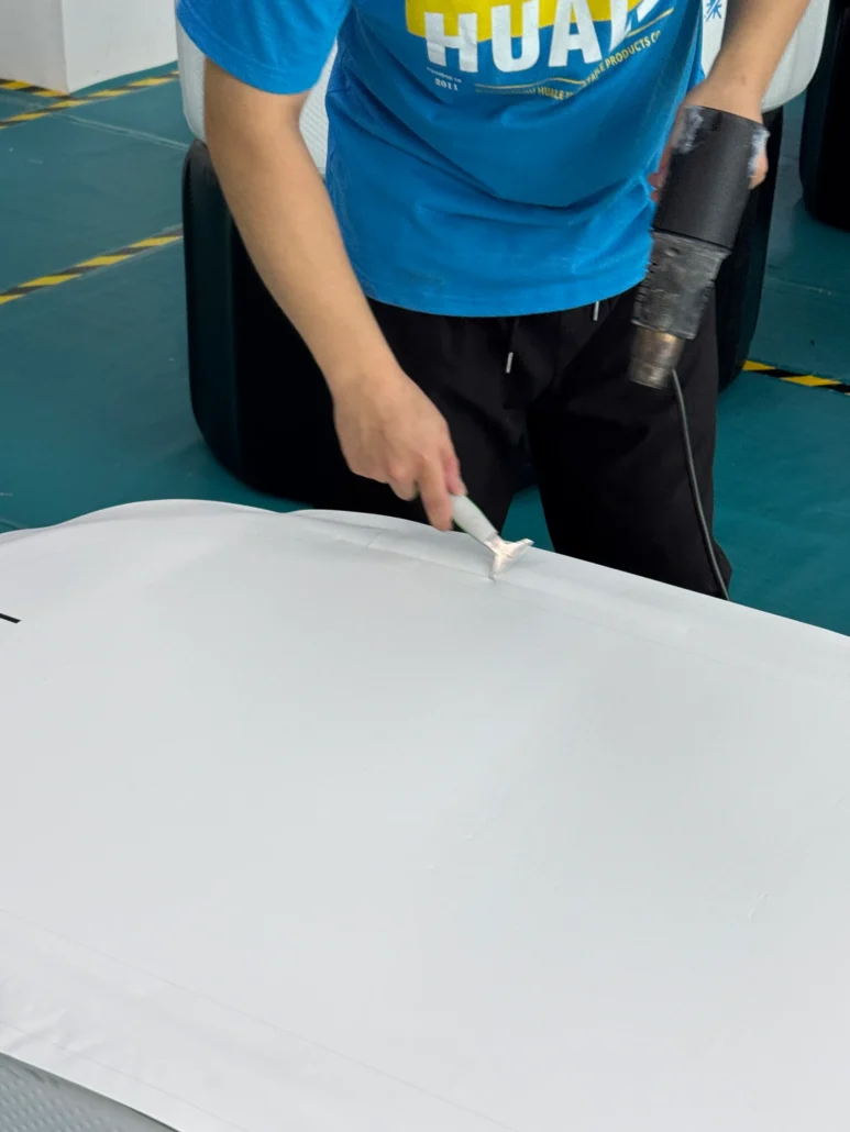 Man using a heat tool and applying sealant to a white material surface in a workshop setting.