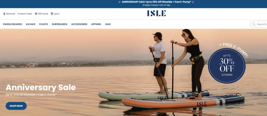 Two people paddleboarding on calm water during sunset with text promoting an anniversary sale offering up to 30% off sitewide and a free e-pump.