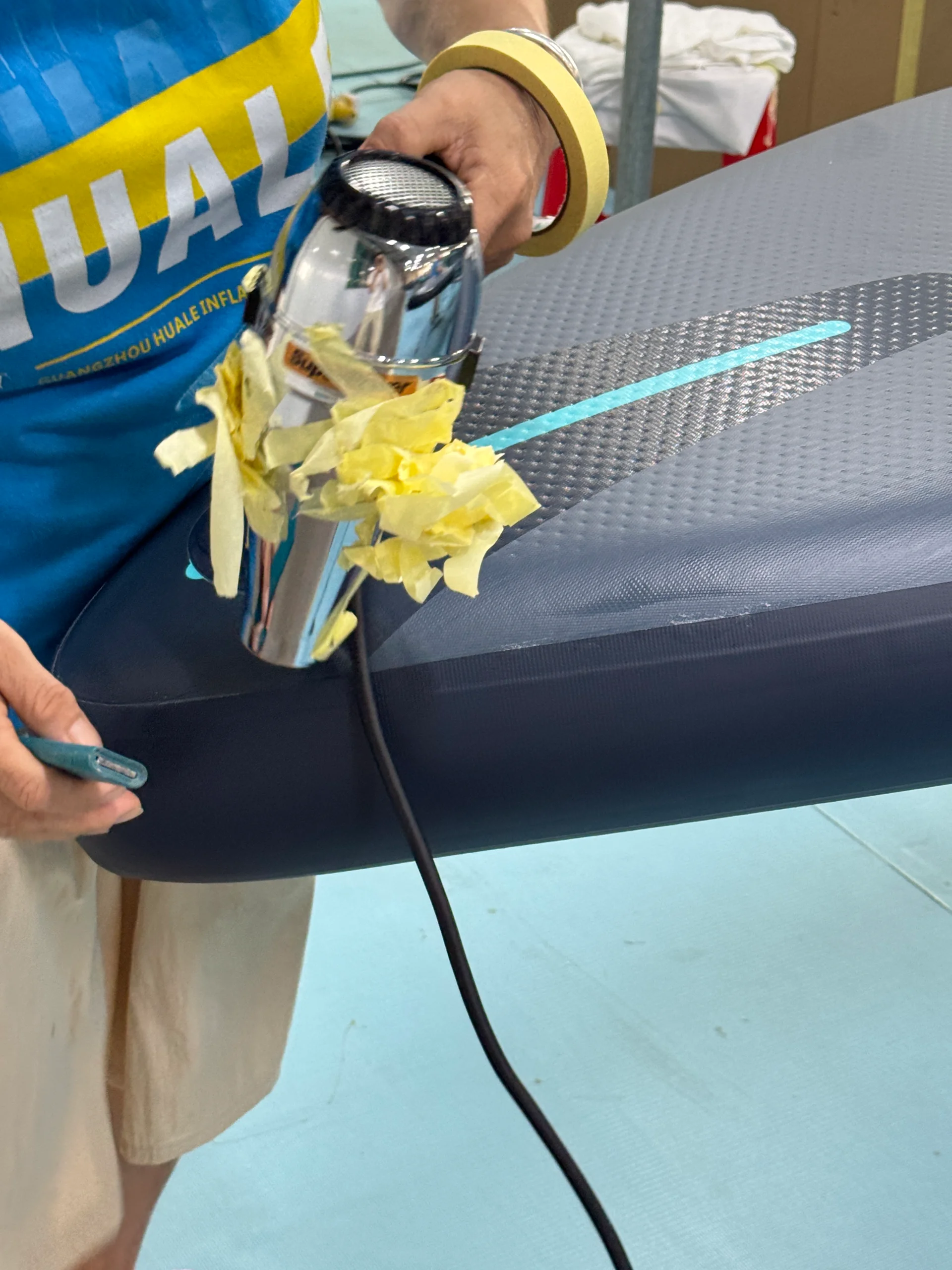 Person using a hair dryer with yellow tape to heat an inflatable raft with a textured surface.