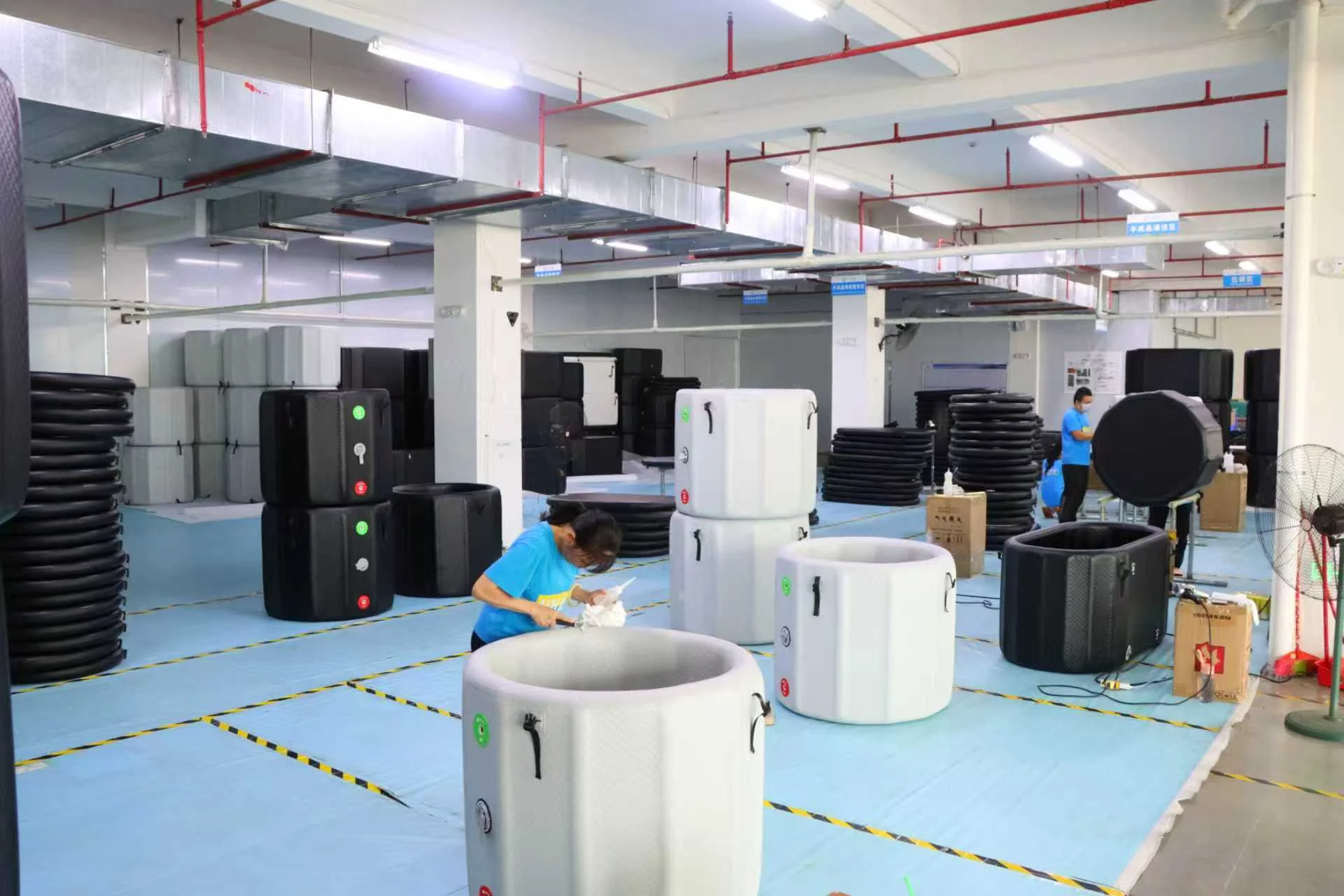 Factory setting with workers assembling portable spa units, surrounded by spa components and equipment in a spacious production area.