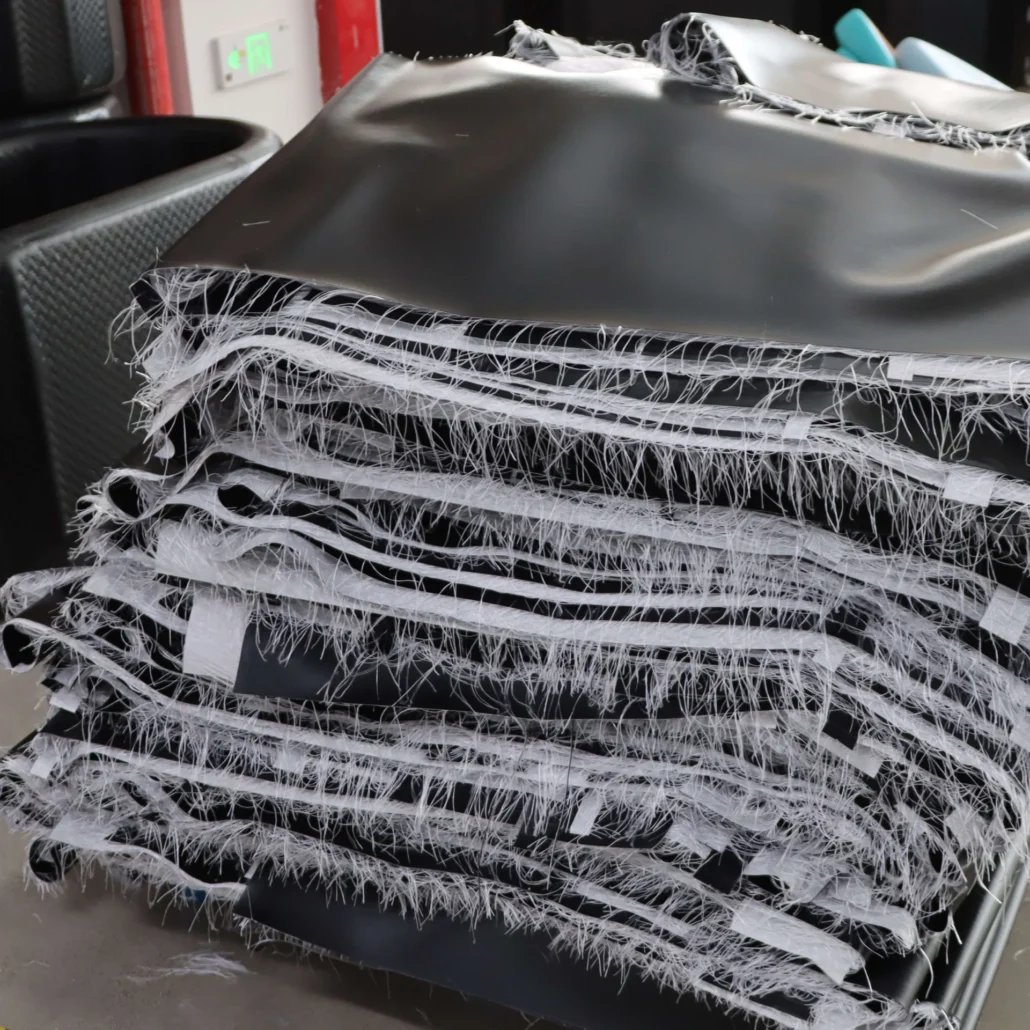 Close-up of a stack of black fabric pieces with frayed edges in a workshop setting.