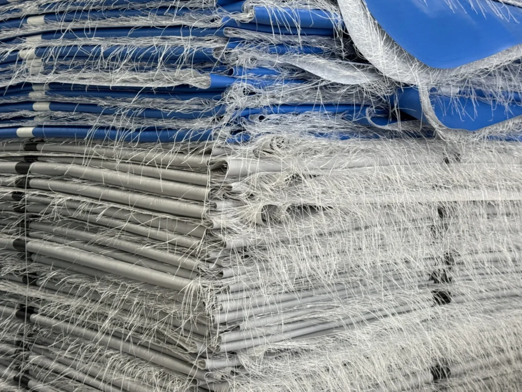 A close-up view of stacked fiberglass mats with visible fibers protruding, showcasing industrial materials in a warehouse setting.