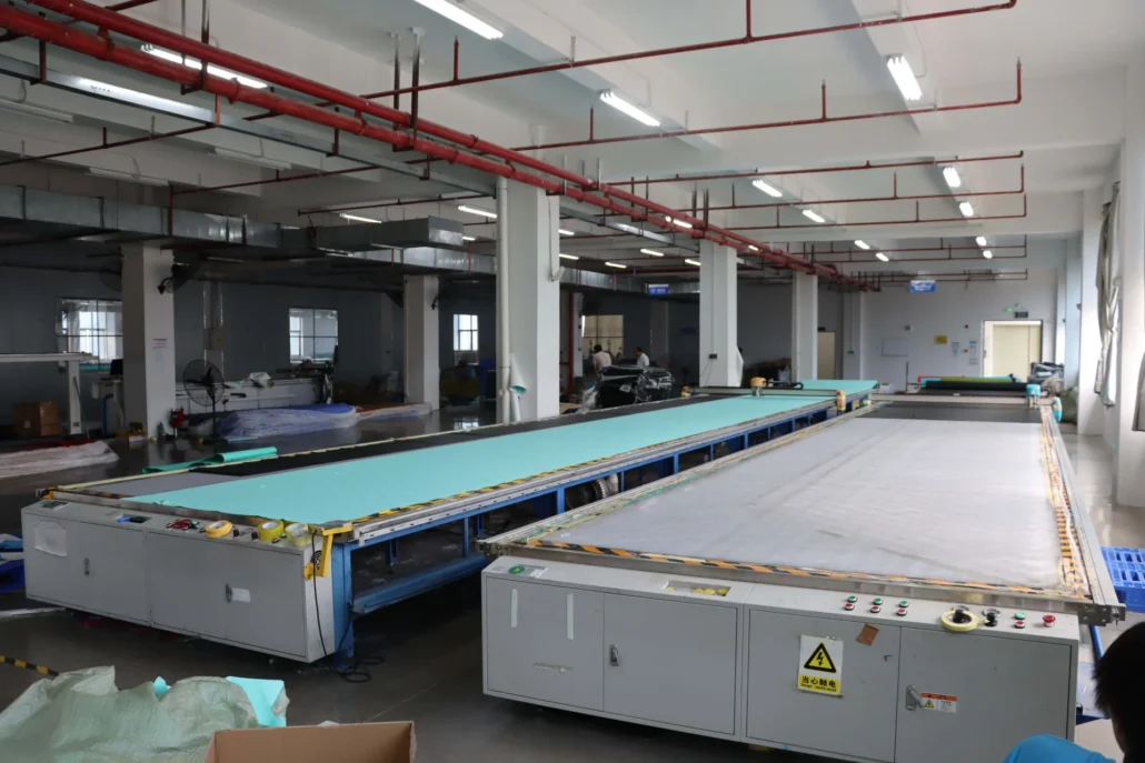 Interior of a textile factory showing a long production line with machinery and fabric rolls on tables.