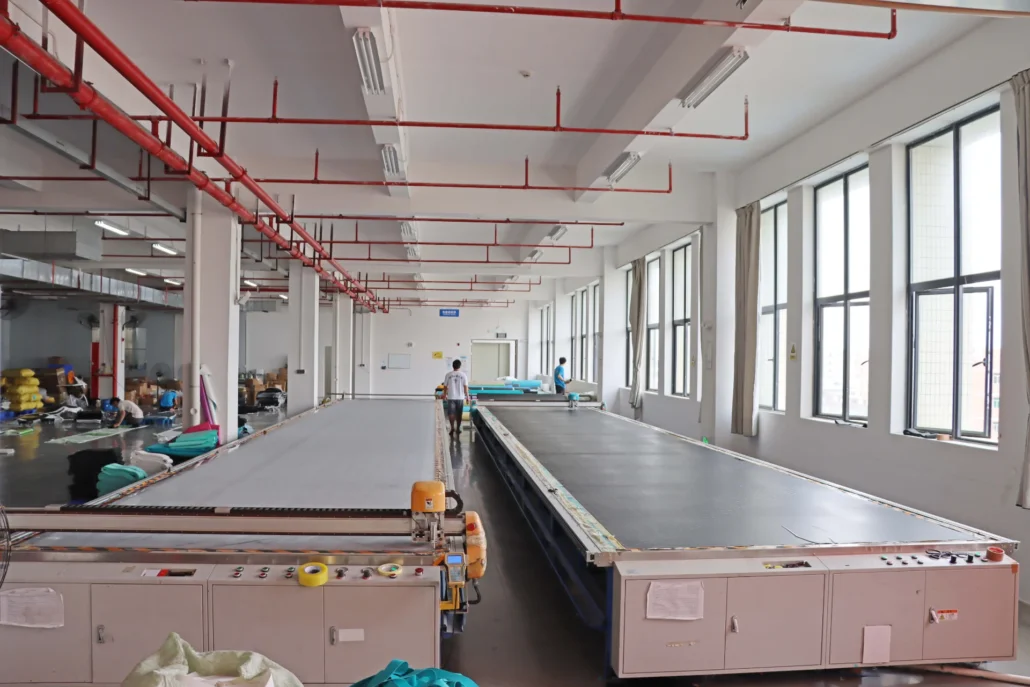Interior of a textile production factory featuring large machinery and workers in a spacious, well-lit environment.
