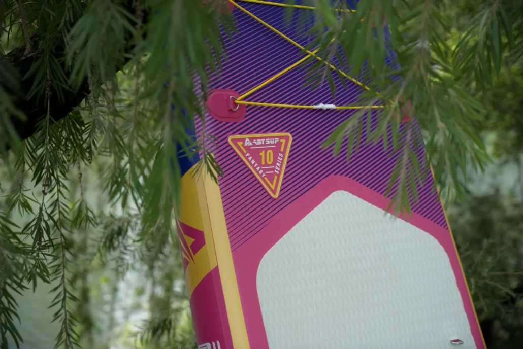 Close-up view of a colorful paddleboard with vibrant patterns and a '10 Fantasy Series' marking, partially obscured by tree branches.