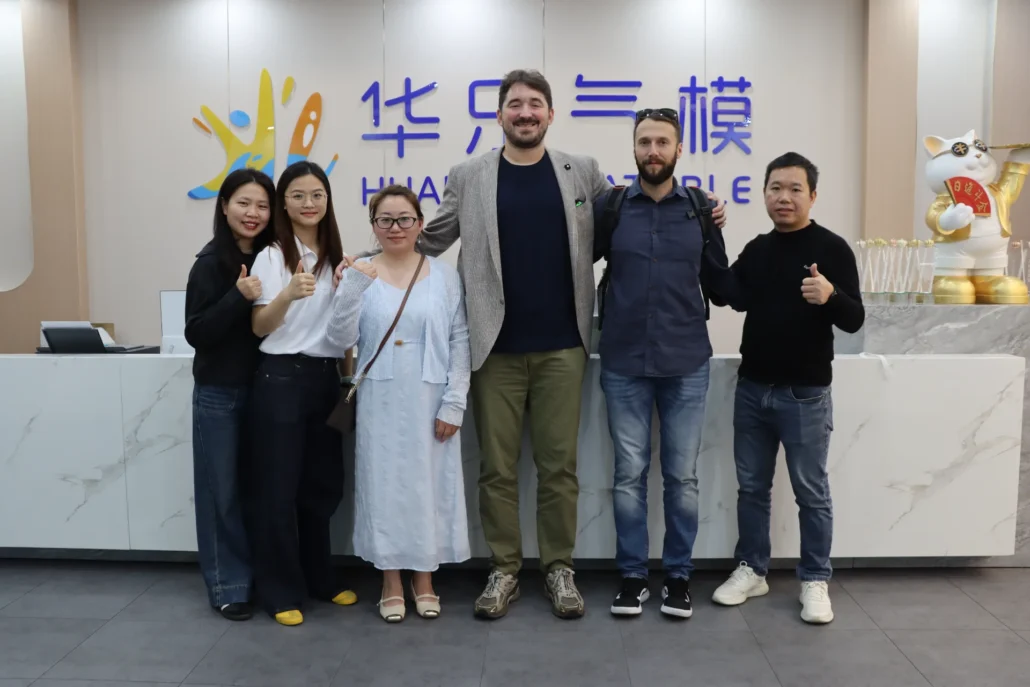 A group of six people posing together at the Huaxu headquarters. The background displays the logo and a decorative golden cat figure.