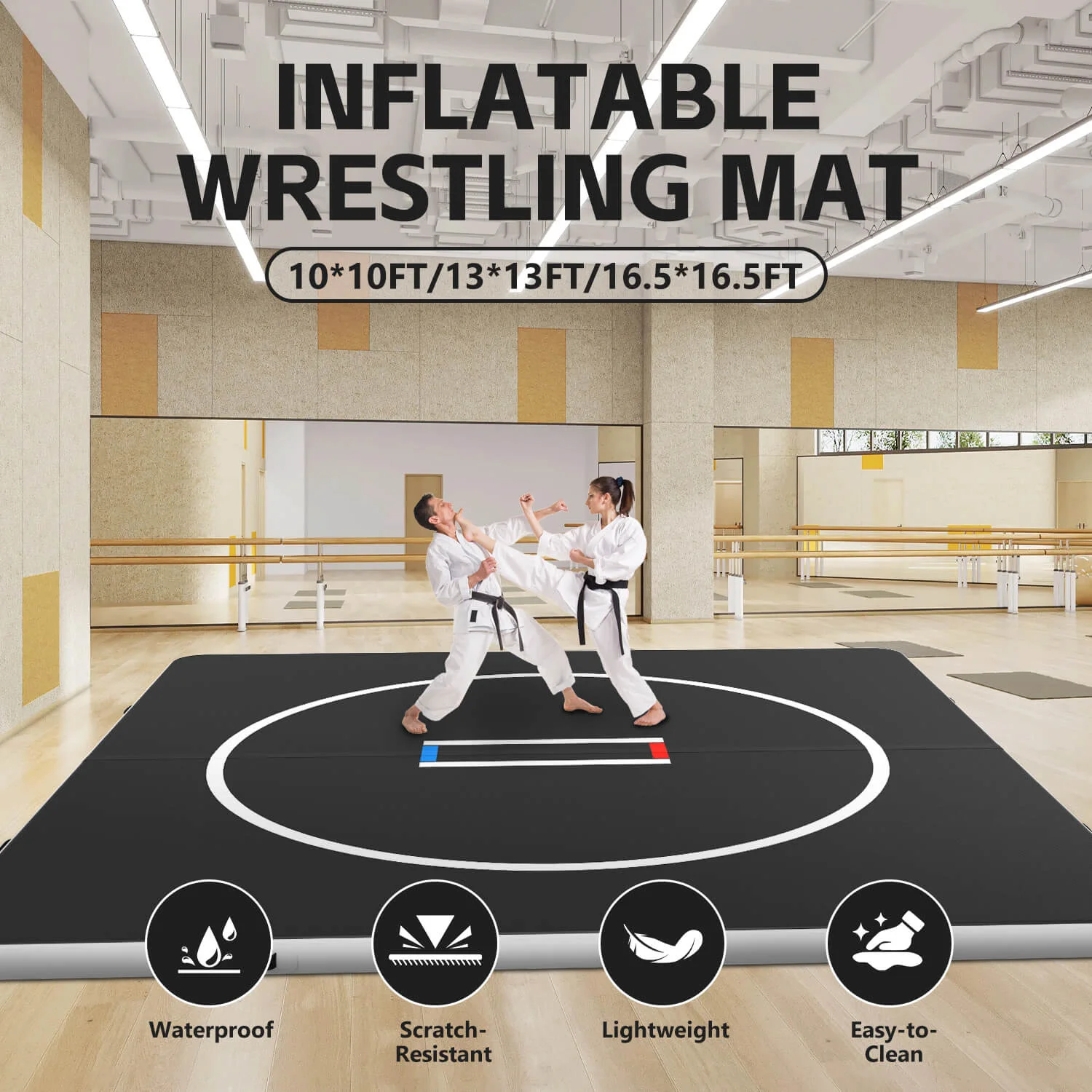 Two martial artists practicing on a black inflatable wrestling mat with white perimeter lines inside a spacious indoor facility.