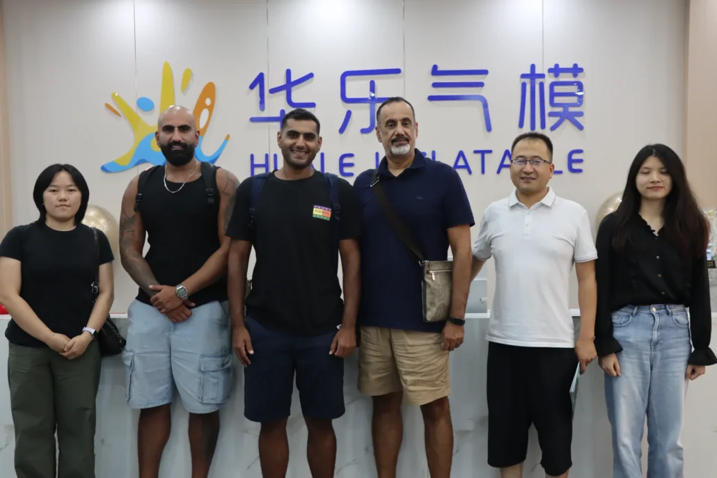 A group of six people standing in a row at the Huile Inflatables office, smiling at the camera with a branded backdrop.