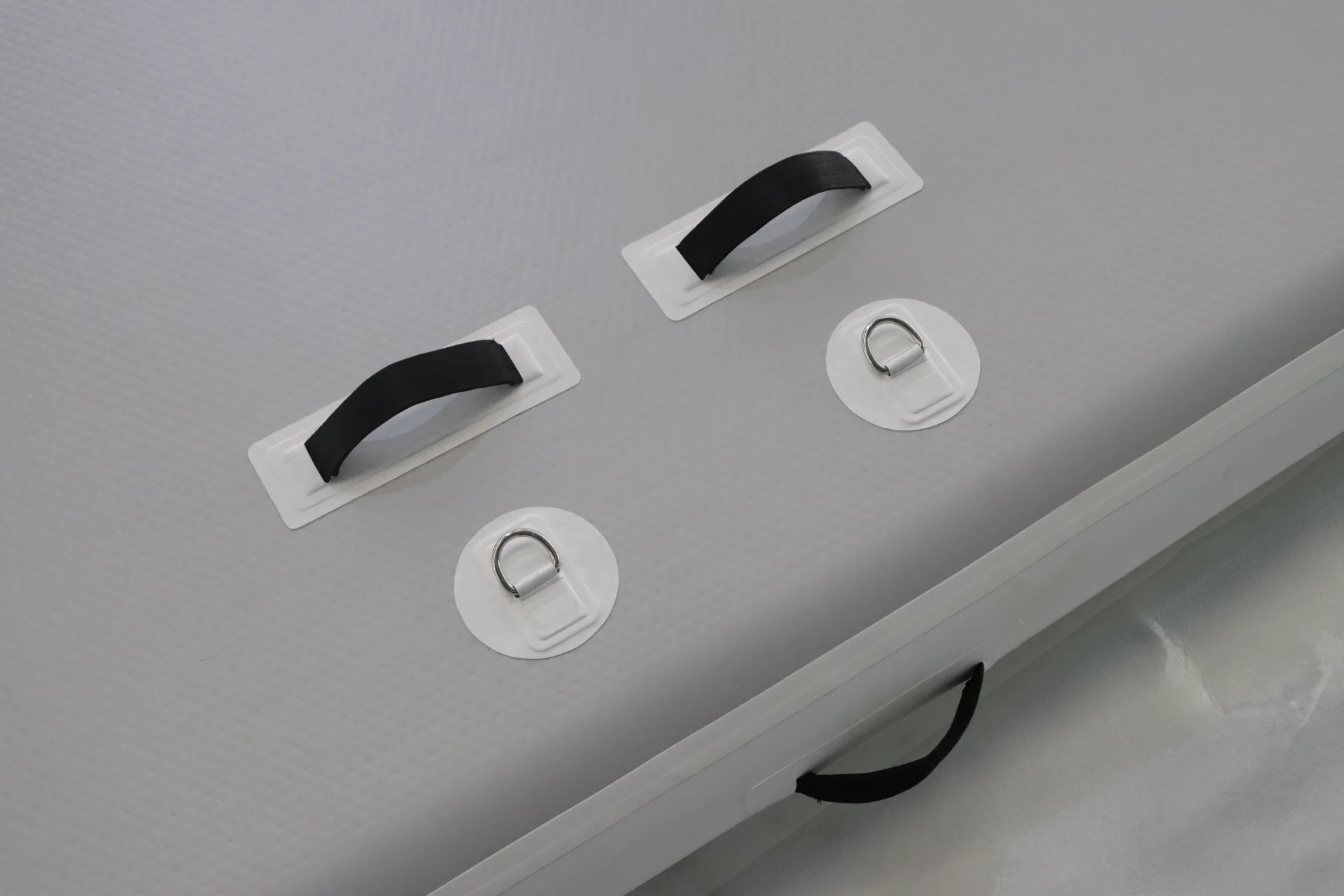 Close-up view of black handles and white D-rings on a gray inflatable mat designed for portability and utility.