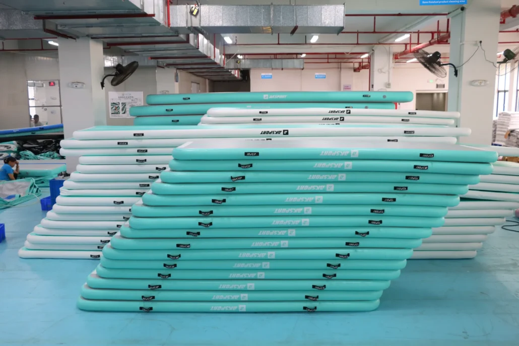 Stacks of turquoise and white paddleboards arranged in a factory production area with industrial features and equipment.