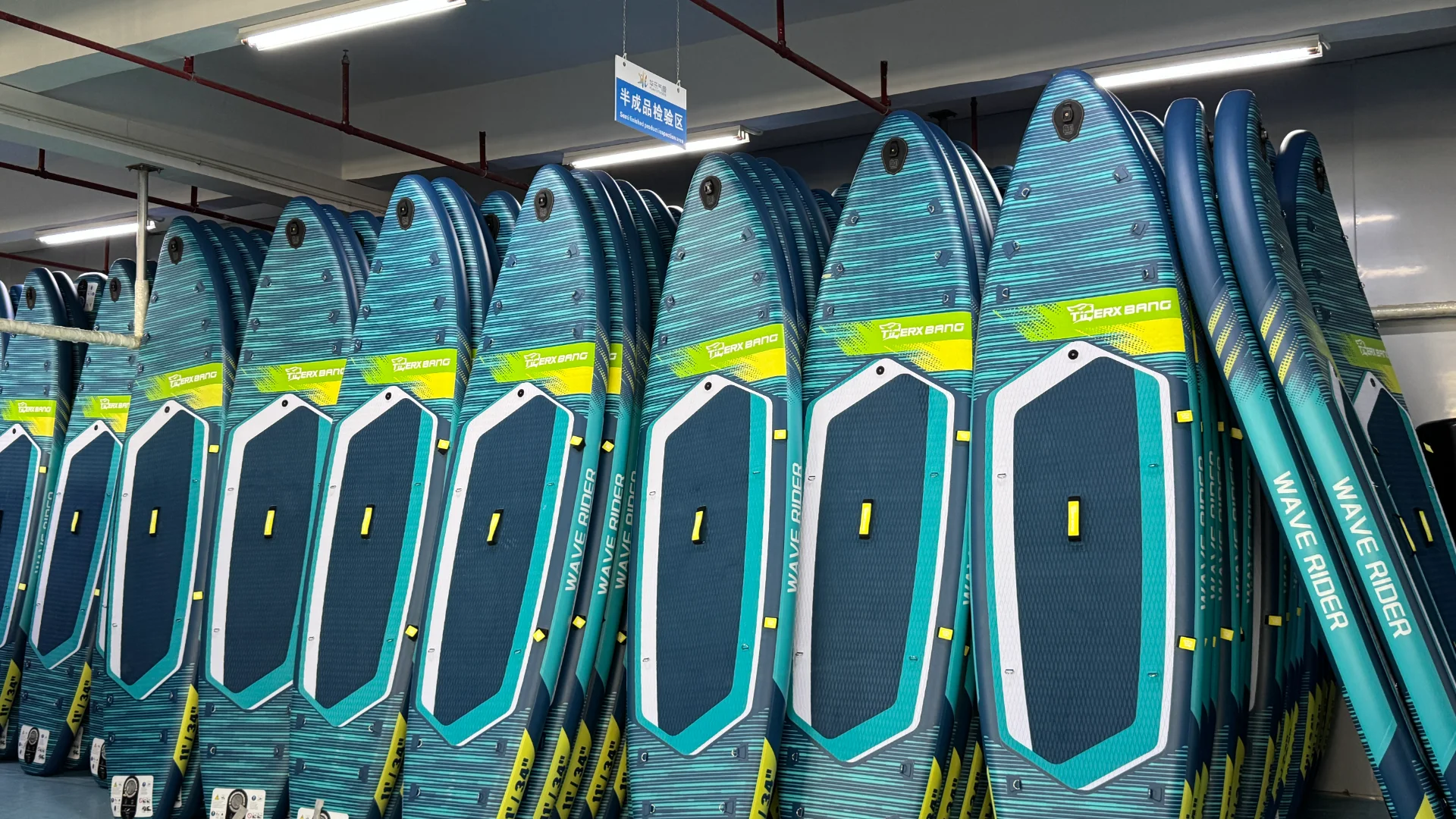 Multiple blue and green paddleboards labeled 'Wave Rider' stacked upright in a storage facility with bright overhead lights.