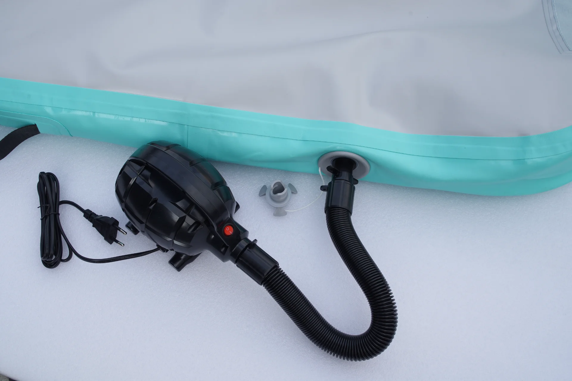 Black electric air pump connected to an inflatable mat with a black hose and power cord on a white surface.