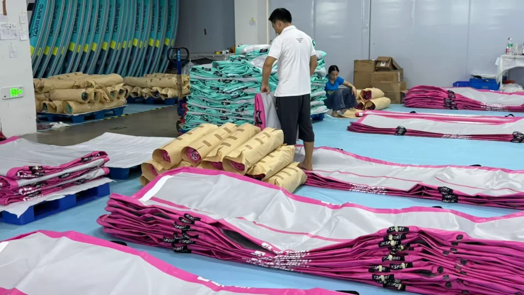Workers in a factory assembling inflatable paddleboards with colorful materials and equipment.
